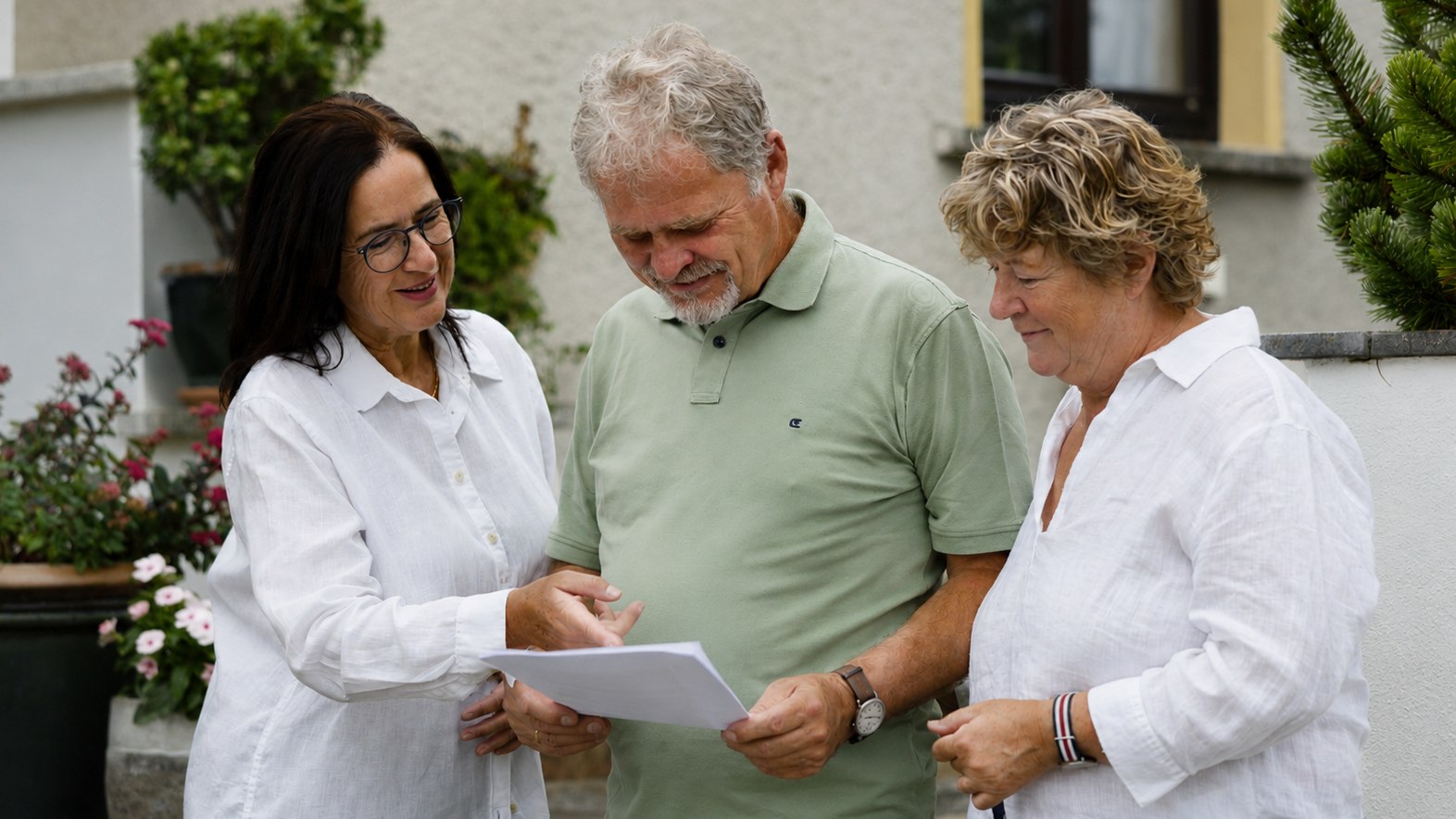 Drei Personen besprechen gemeinsam Unterlagen vor einem Haus